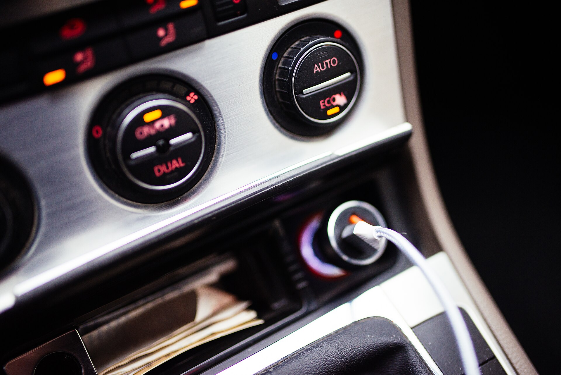 Car dashboard controls with a phone charging cable at night