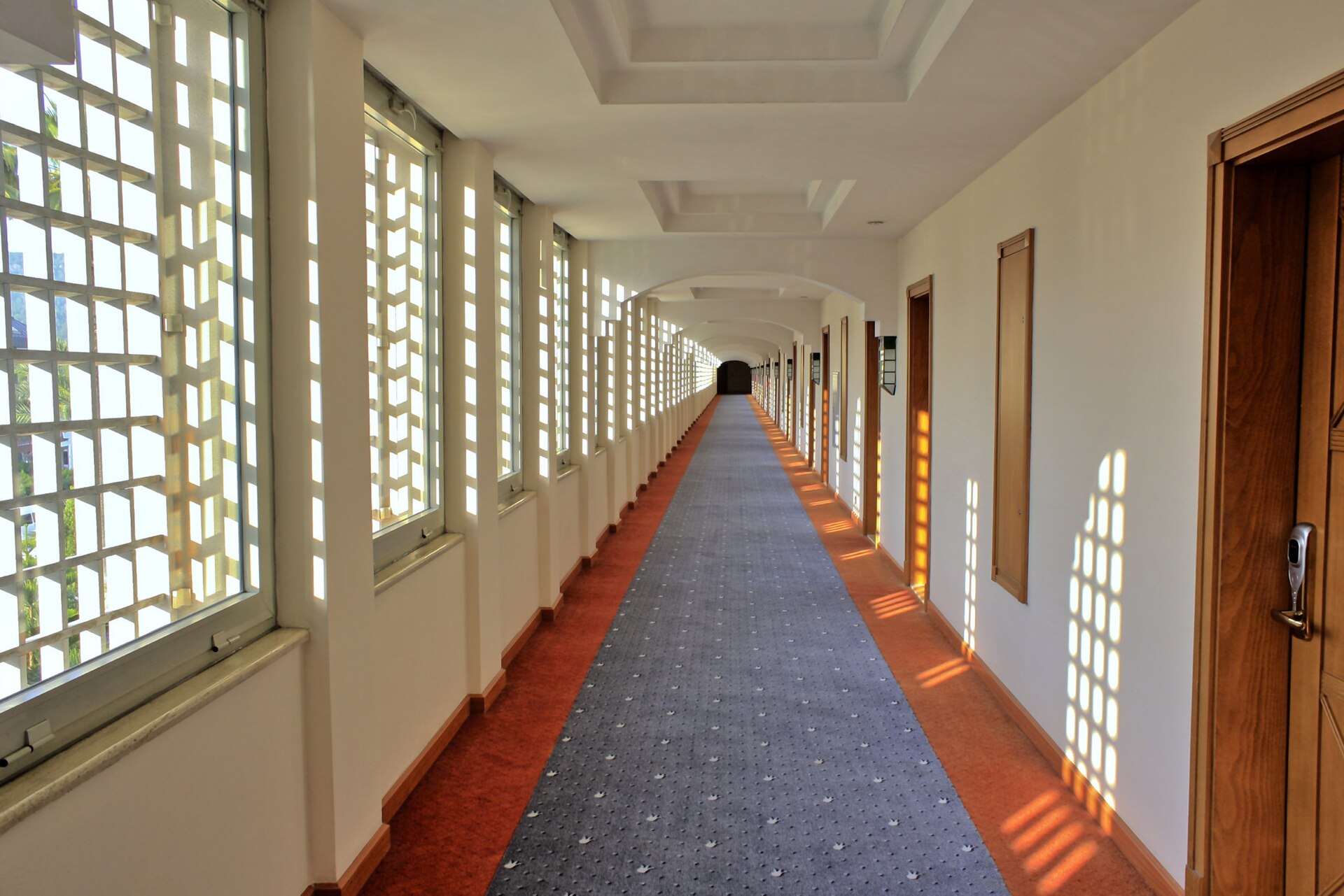 Sunlit hotel corridor with carpet, patterned windows and wooden doors