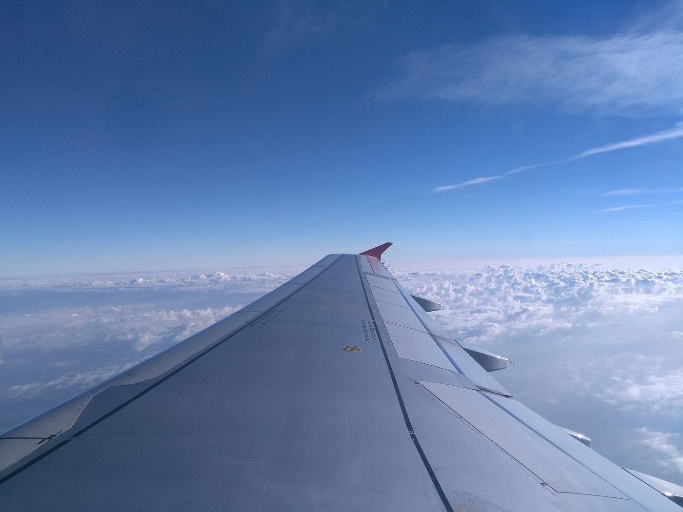 Airplane wing seen from a passenger window above clouds and blue sky