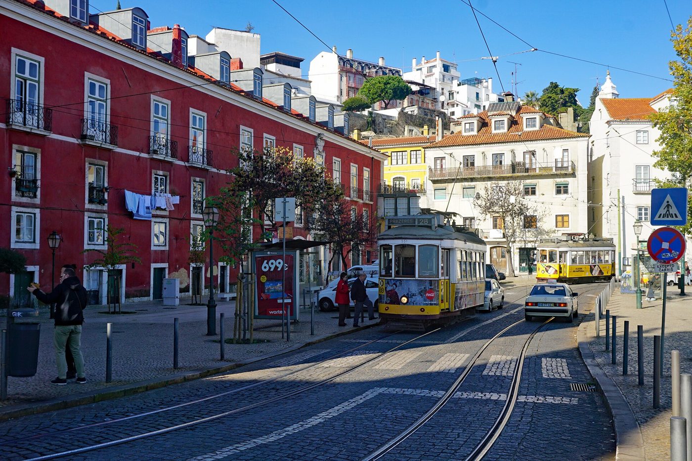 Yellow tram climbing a narrow cobbled street between tiled buildings in Lisbon's Alfama district